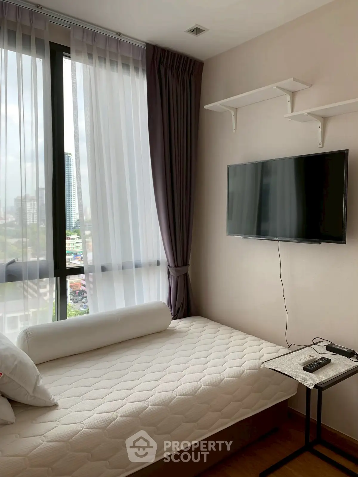 Modern bedroom with city view, wall-mounted TV, and cozy mattress.