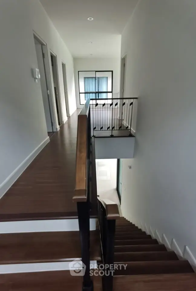 Modern interior hallway with wooden flooring and railing, leading to multiple rooms.
