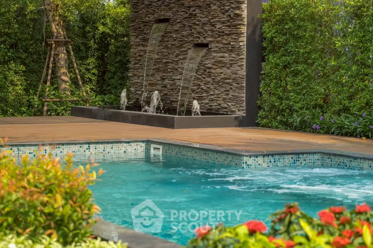 Luxurious outdoor pool with elegant stone waterfall feature and lush greenery.