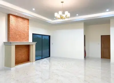 Spacious living room with elegant chandelier and brick fireplace, featuring large sliding glass doors.
