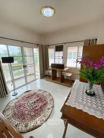 Bright living room with large windows and elegant decor, featuring a round rug and a scenic view.