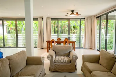 Spacious living room with cozy seating and large windows overlooking lush greenery.