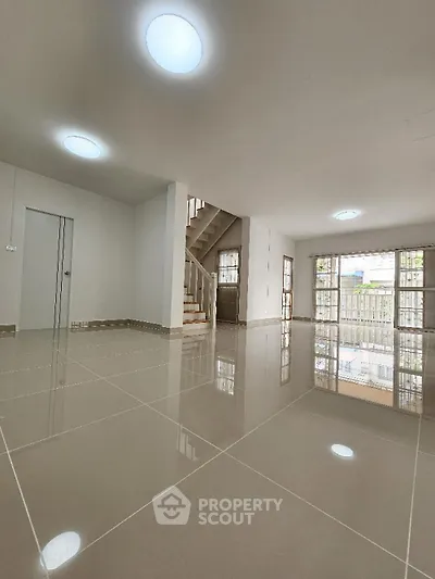 Spacious and bright living area with glossy tiled flooring, modern recessed lighting, and an elegant staircase leading to the upper level, perfect for luxurious living.