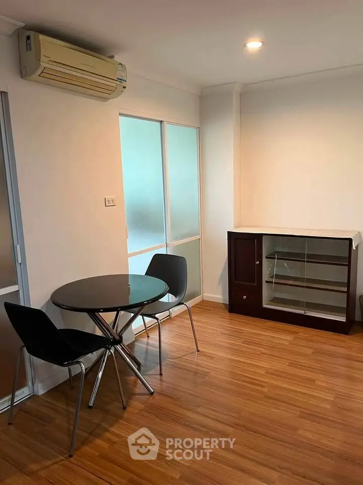 Modern living room with sleek furniture and wooden flooring, featuring a compact dining area and air conditioning.