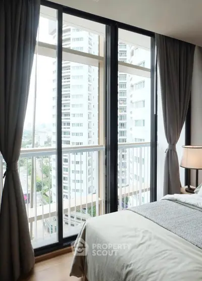 Modern bedroom with floor-to-ceiling windows and city view, featuring elegant curtains and cozy bedding.
