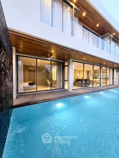 Luxurious modern home with stunning poolside view and expansive glass windows.