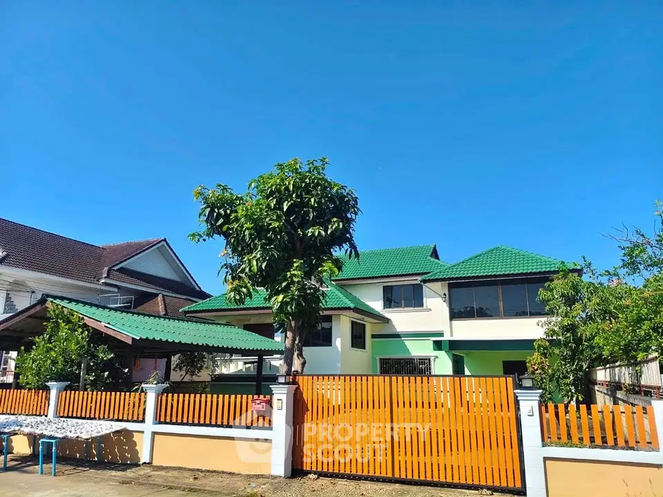Charming two-story house with green roof and wooden fence under clear blue sky.
