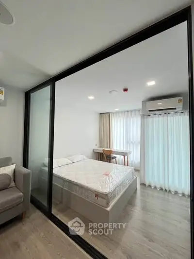 Modern bedroom with glass partition, cozy bed, and natural light from large window.