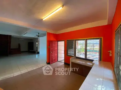 Spacious open-plan living area with vibrant orange walls and large windows for natural light.