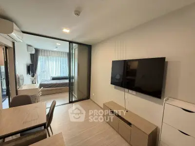 Modern living room with open layout and bedroom view, featuring sleek furniture and large TV.