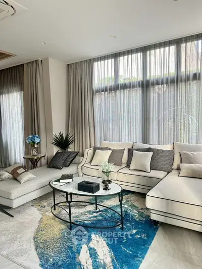 Luxurious living room with elegant sofa and modern decor, featuring large windows and stylish rug.