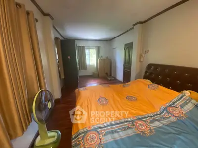 Spacious bedroom with vibrant bedding and natural light, featuring elegant curtains and wooden flooring.