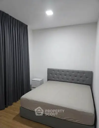 Modern minimalist bedroom with grey upholstered bed and floor-to-ceiling curtains.