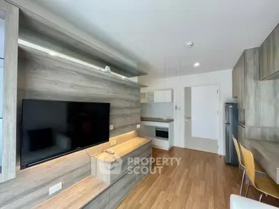 Modern living room with sleek wooden flooring and built-in TV unit, adjacent to a compact kitchen area.