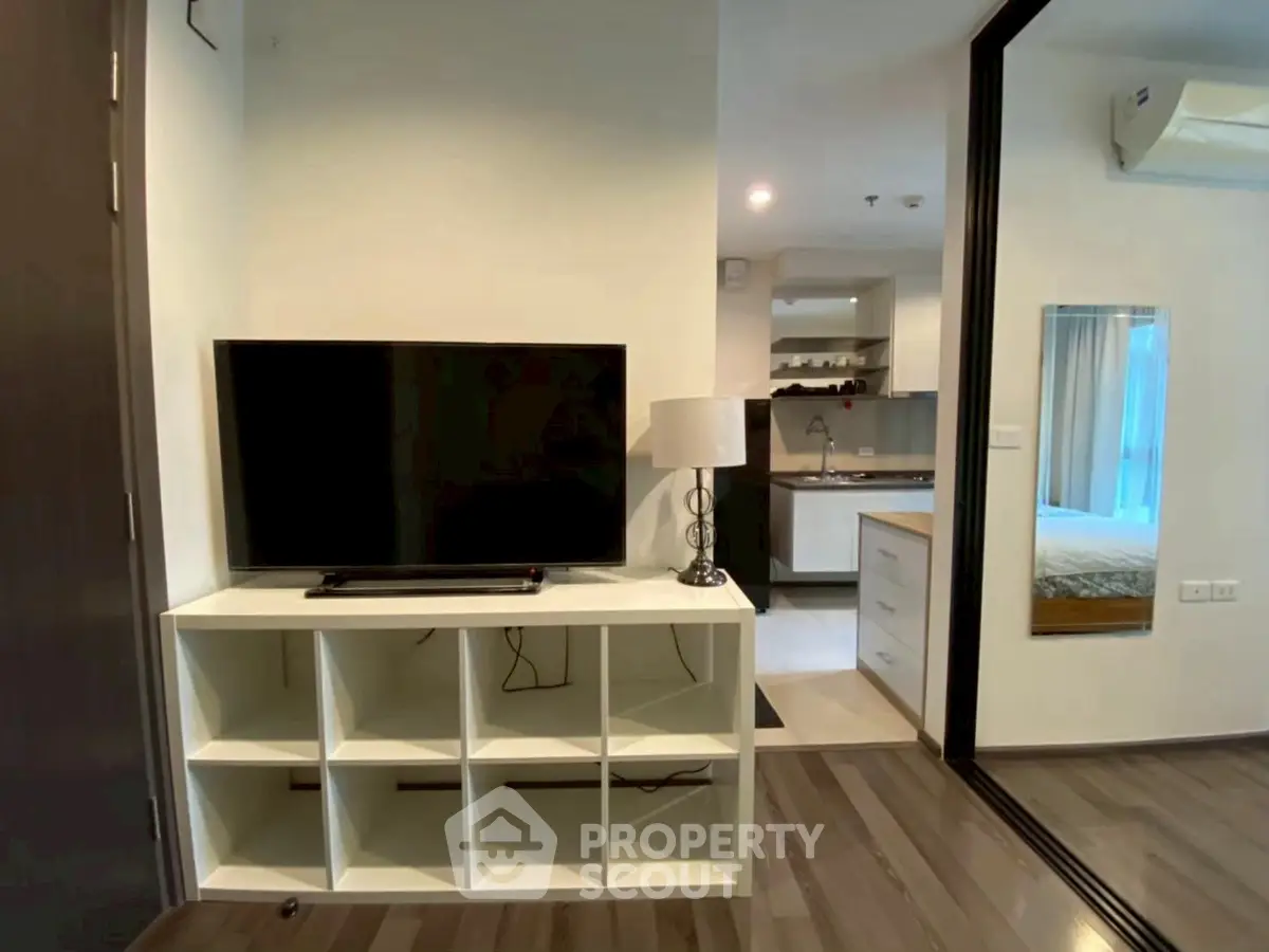 Modern apartment interior with TV, open kitchen, and cozy bedroom view.
