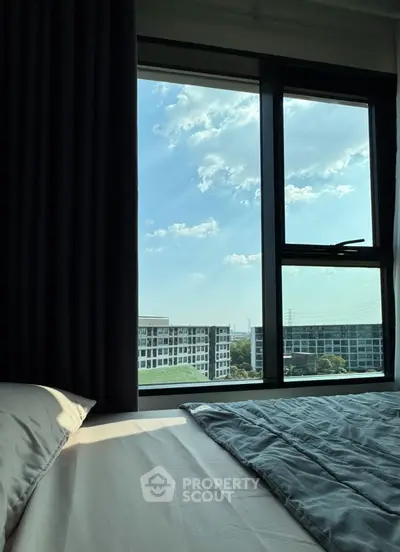 Cozy bedroom with large window offering stunning city view and natural light.