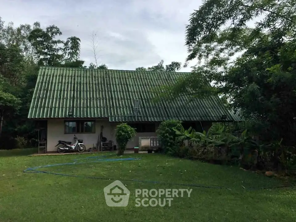 Charming countryside house with green roof surrounded by lush garden and trees, perfect for nature lovers.