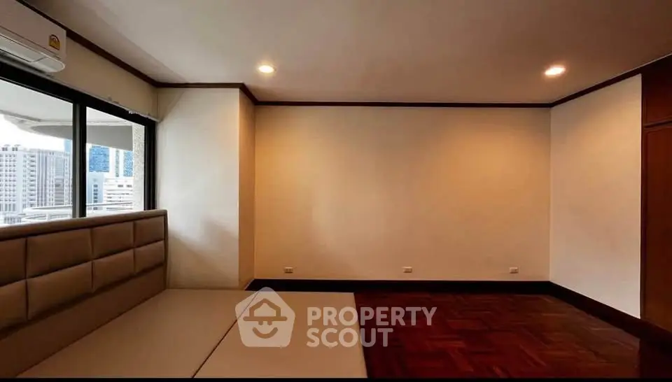 Spacious empty room with wooden flooring and large windows in urban apartment.