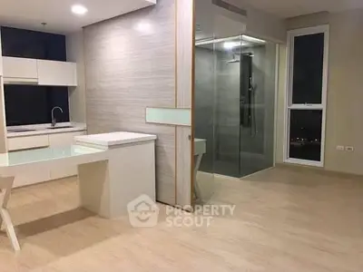 Modern open-plan living space with sleek kitchen and glass-enclosed shower area.