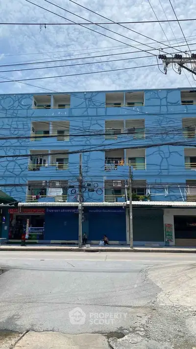 Blue multi-story residential building with street view and retail shops below.