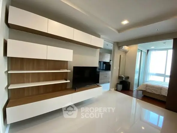 Modern living room with sleek TV unit and view into cozy bedroom