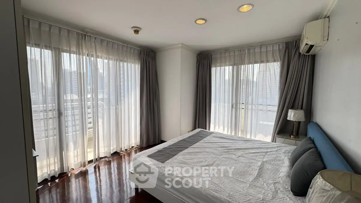 Spacious bedroom with large windows and city view, featuring elegant curtains and modern decor.