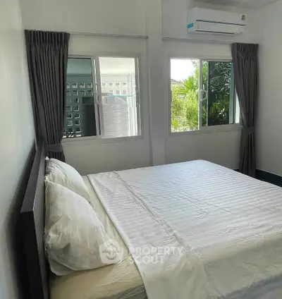 Cozy bedroom with large windows and air conditioning, perfect for relaxation and comfort.