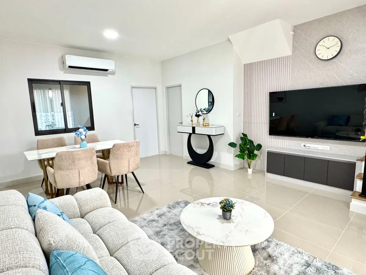 Spacious modern living room with elegant decor and dining area, featuring a large TV and stylish furniture.