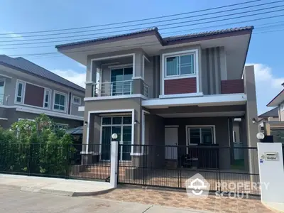 Modern two-story house with balcony and gated driveway in suburban neighborhood.