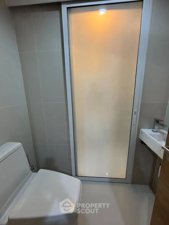 Modern bathroom with sleek design featuring a frosted glass door and contemporary fixtures.