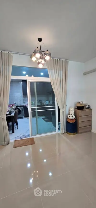 Spacious living room with modern lighting and sliding glass doors leading to a stylish kitchen.