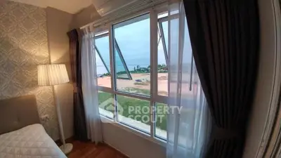 Cozy bedroom with stunning ocean view through large windows, featuring elegant curtains and a stylish floor lamp.