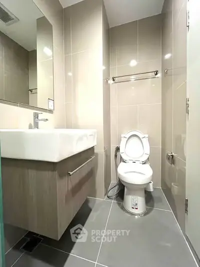 Modern bathroom with sleek fixtures and neutral tiles, featuring a contemporary sink and toilet.