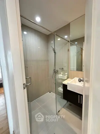 Modern bathroom with glass shower and sleek vanity in contemporary apartment.