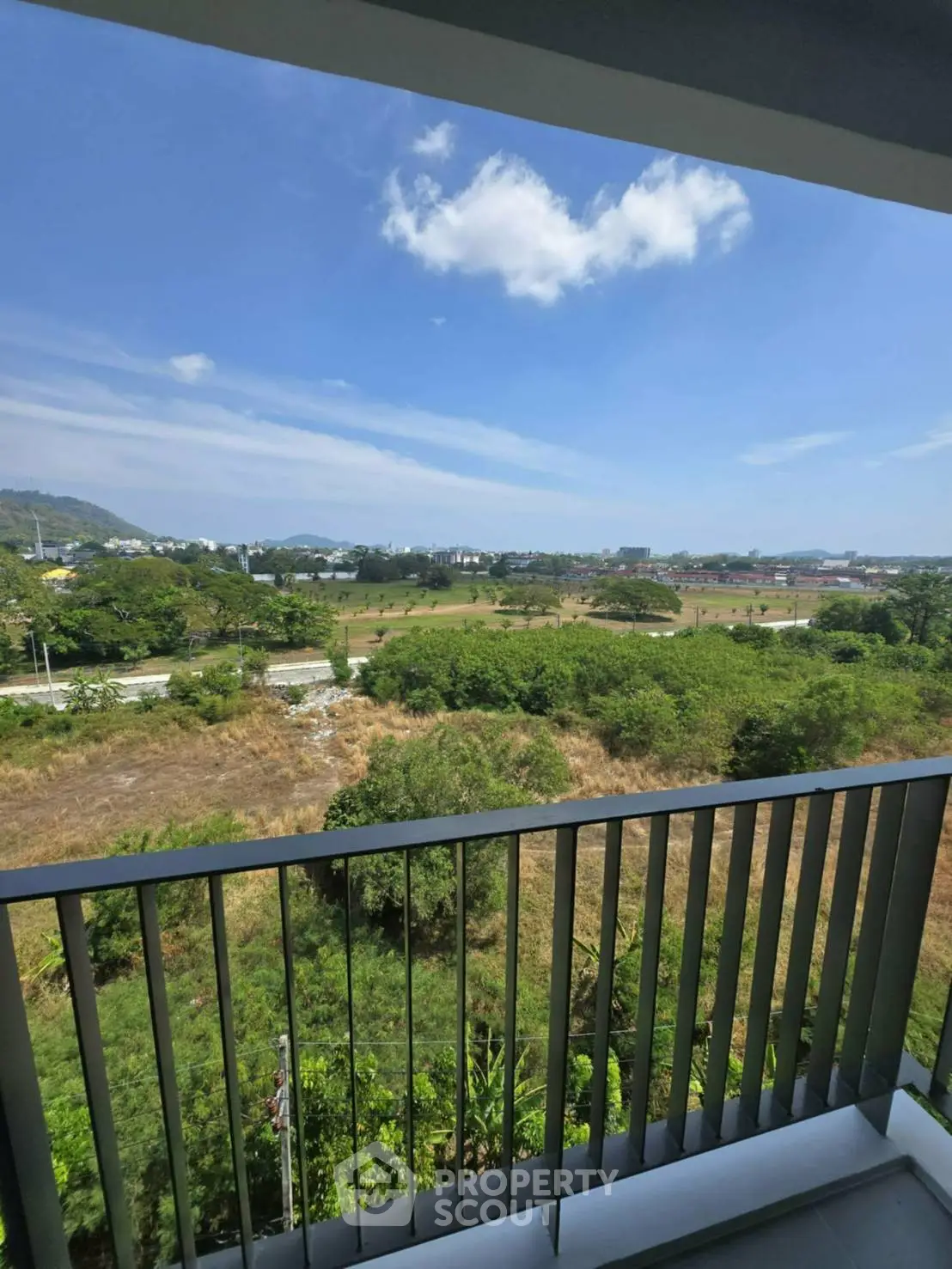 Stunning balcony view overlooking lush greenery and distant hills under a clear blue sky.