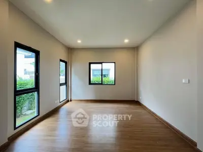 Spacious empty room with wooden flooring and large windows in modern home.