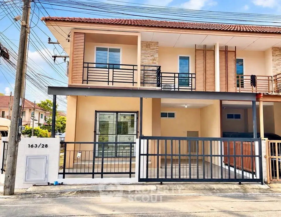 Modern two-story house with gated entrance and balcony in a suburban neighborhood.
