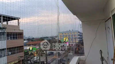 Urban balcony view with safety netting overlooking bustling street and cityscape.