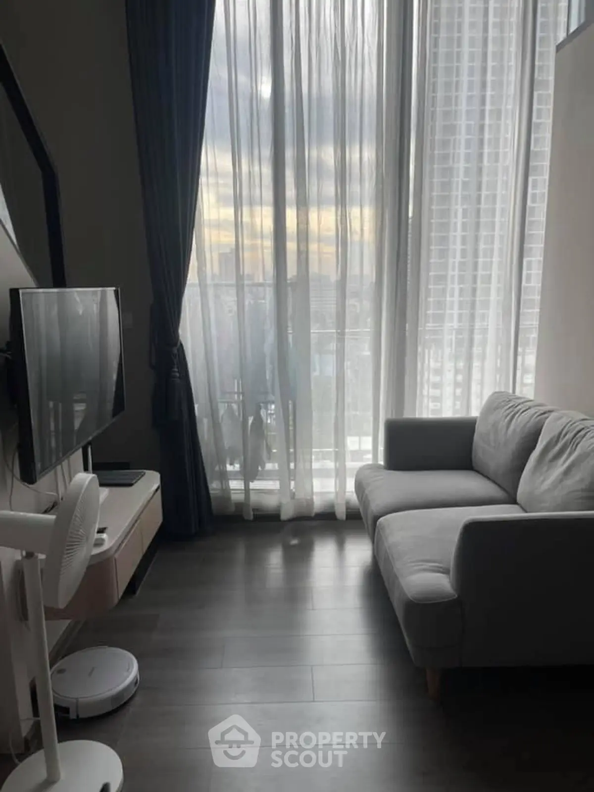 Modern living room with floor-to-ceiling windows and city view, featuring sleek furniture and natural light.