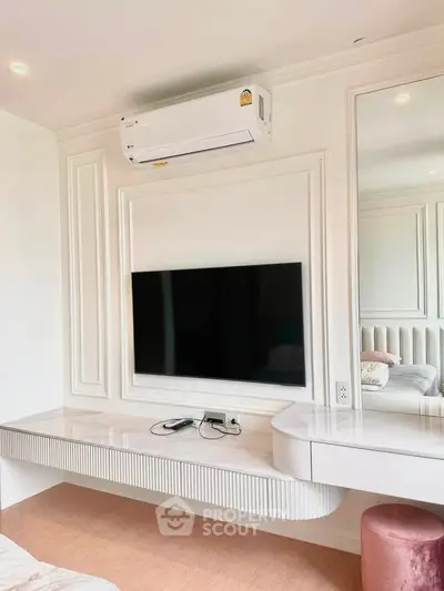 Modern bedroom with wall-mounted TV and air conditioning, featuring elegant white paneling and a sleek vanity desk.