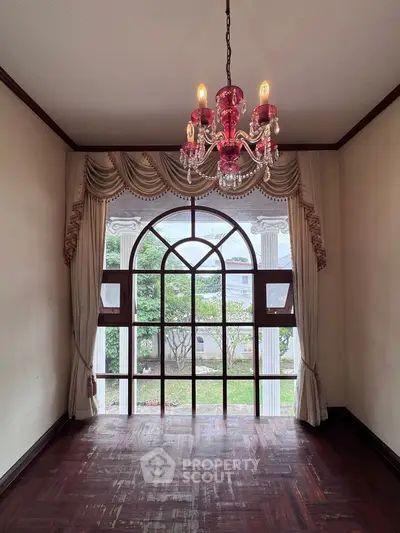 Elegant room with chandelier and large arched window overlooking garden