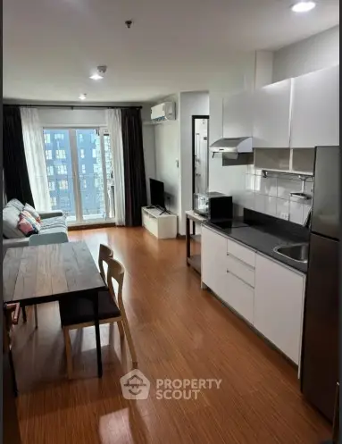 Modern open-layout living room and kitchen with wooden flooring and natural light.