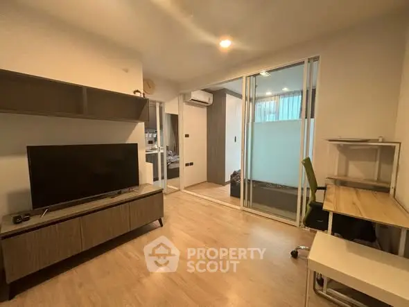 Modern living room with TV, desk, and sliding glass doors in a stylish apartment.