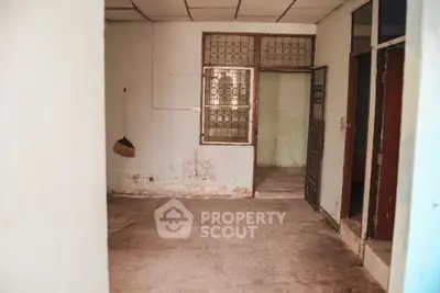 Spacious room with potential for renovation, featuring large window and open doorway.