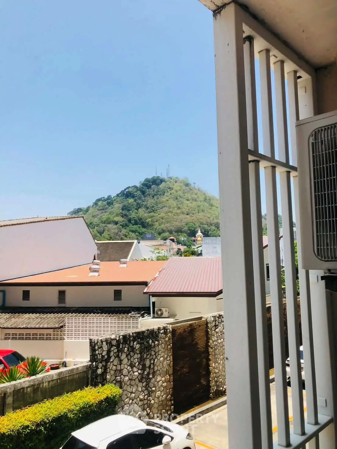 Scenic view from a balcony overlooking rooftops and a lush green hill, perfect for serene living.