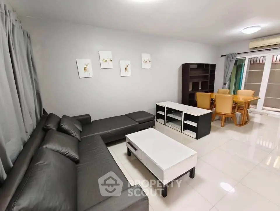 Spacious modern living room with sleek black sofa and elegant dining area.