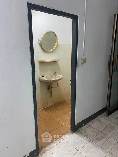 Compact bathroom with round mirror and basic sink in a minimalist setting.