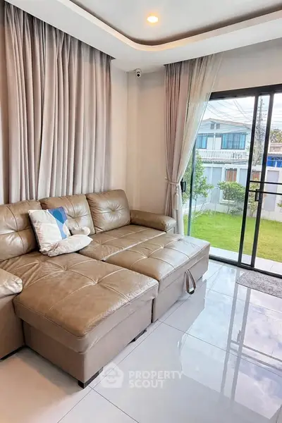Spacious living room with leather sofa and garden view through sliding glass doors.