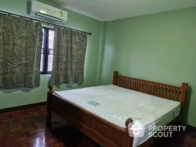 Spacious bedroom with wooden bed frame and green walls, featuring air conditioning and parquet flooring.