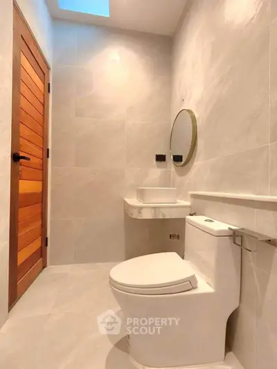 Modern bathroom with sleek design and wooden door, featuring a round mirror and elegant fixtures.